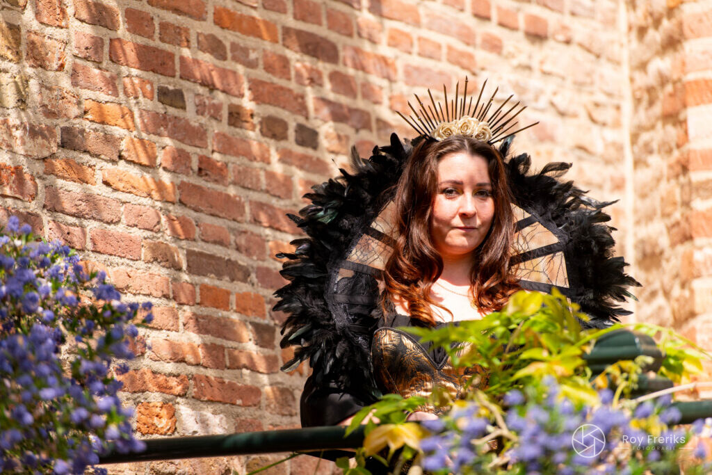 Vrouw met zwarte verenkraag en gouden kroon bij de kasteelmuur