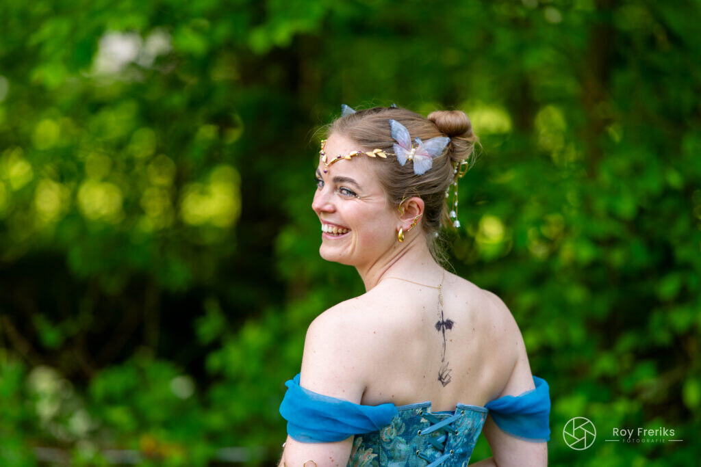 Vrouw in blauwe jurk met vlinder in het haar kijkt opzij