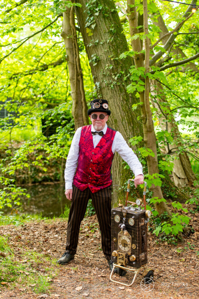 Man in steampunkkleding met hoge hoed en koffer in het bos