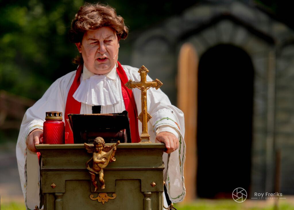 Man als predikant met kruis en lantaarns bij een kerkje