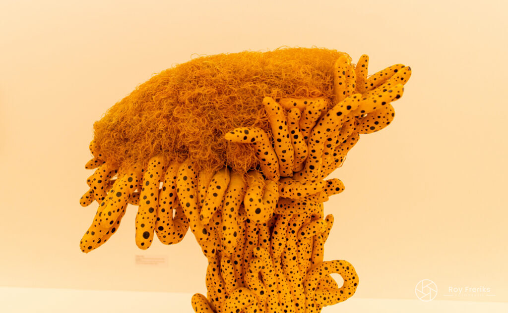 Oranje sculptuur met stippen op witte sokkel