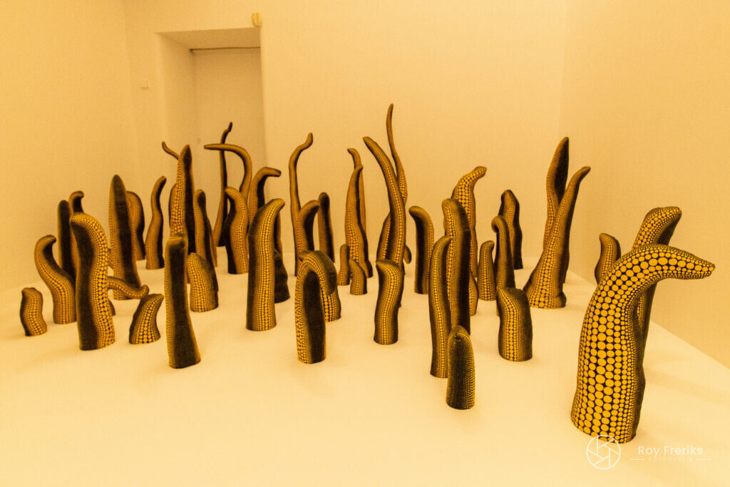 Zwart-gele tentakelvormige sculpturen in een witte zaal