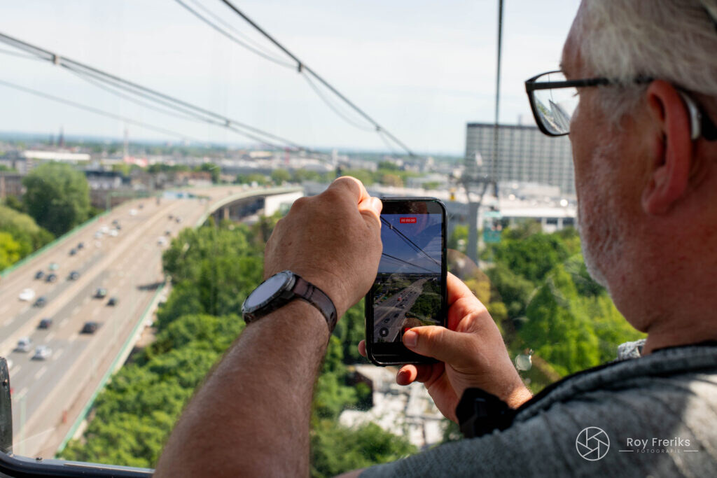 Man fotografeert met zijn telefoon vanuit de kabelbaan