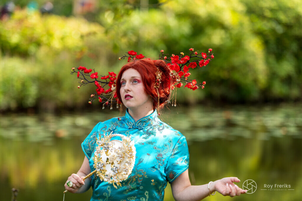 Vrouw in turquoise Chinese jurk met rode bloesem in het haar bij de vijver van Kasteeltuinen Arcen