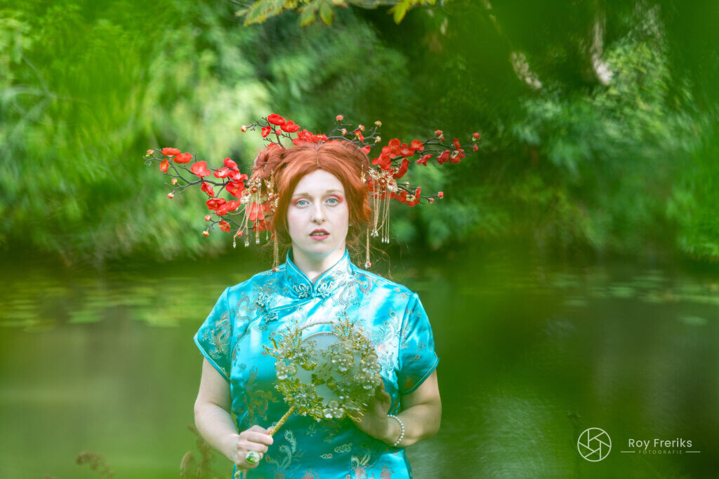 Vrouw in turquoise jurk met rode bloesemkroon tegen een groene achtergrond