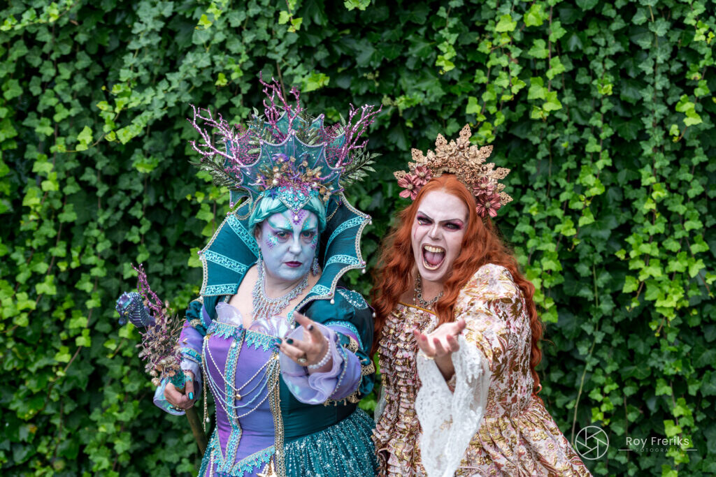 Twee vrouwen in fantasiekostuums met kronen voor een klimopwand