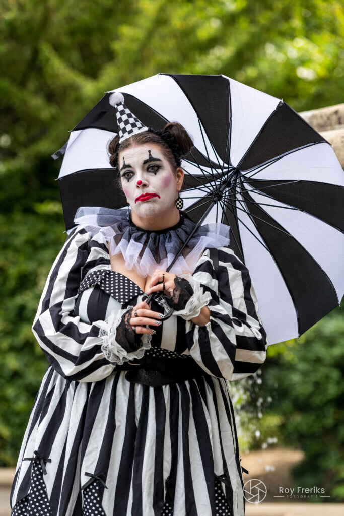 Clown in zwart-wit gestreept kostuum met een gestreepte paraplu