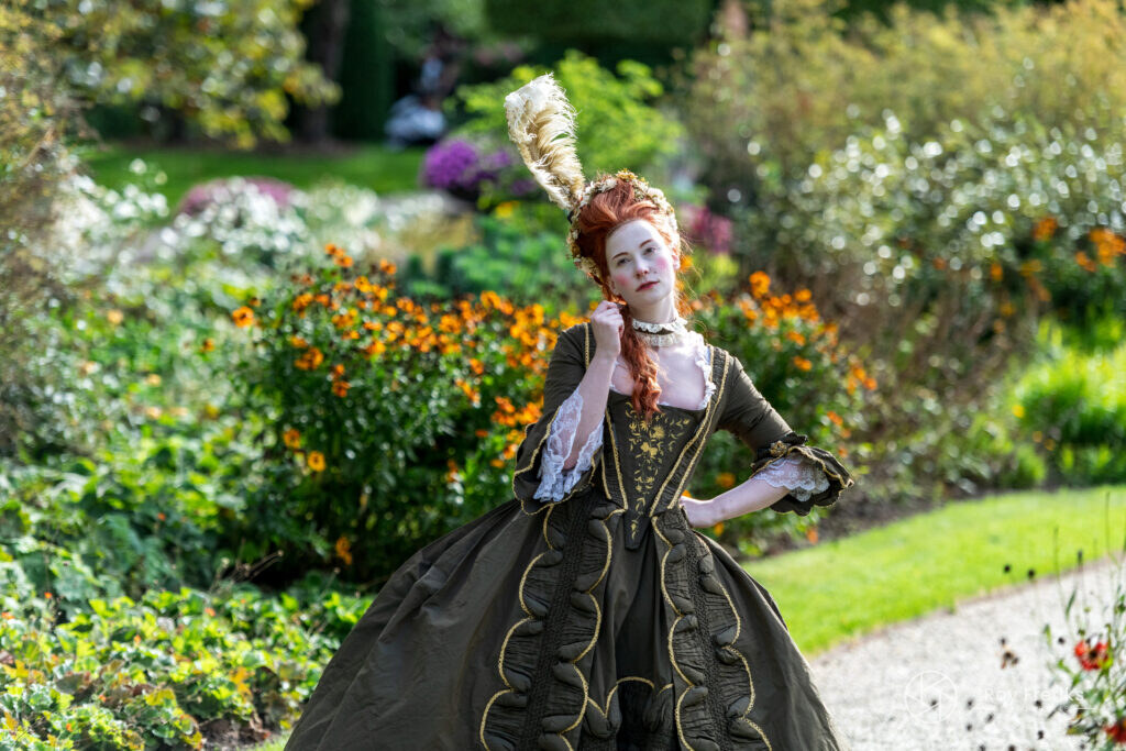 Vrouw in donkere barokjurk tussen de bloemen van de kasteeltuin