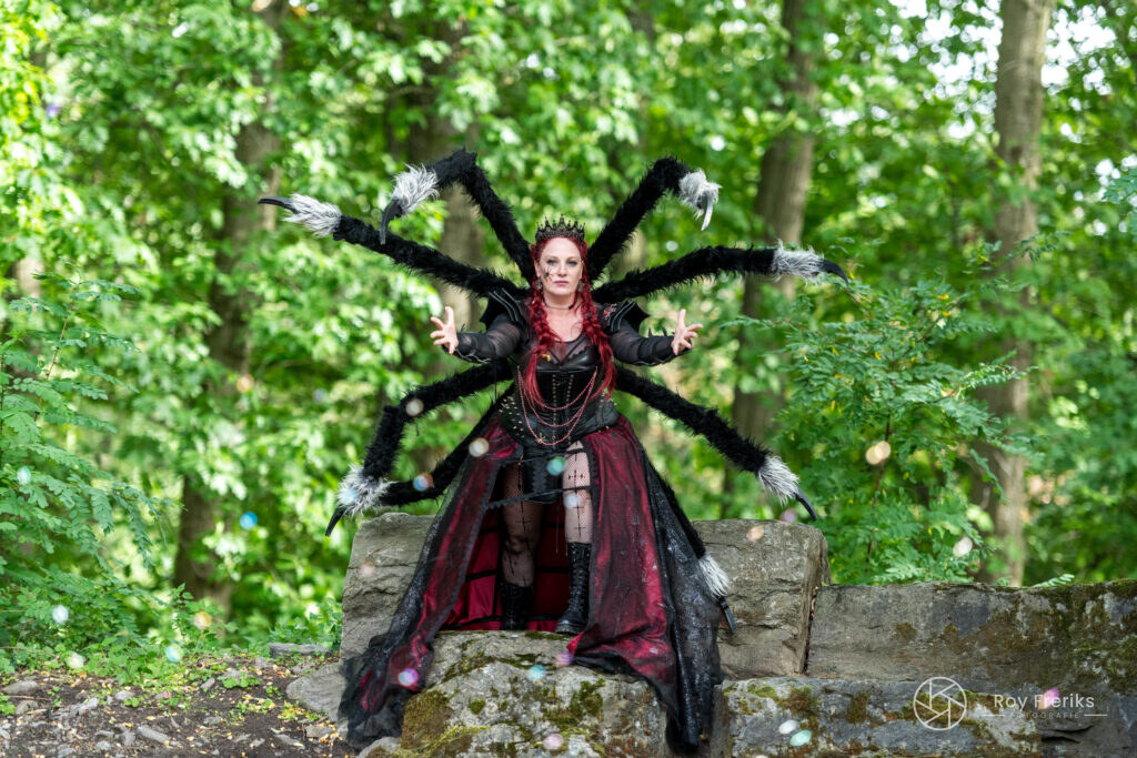 Vrouw in spinnenkostuum met lange poten op een rots in het bos