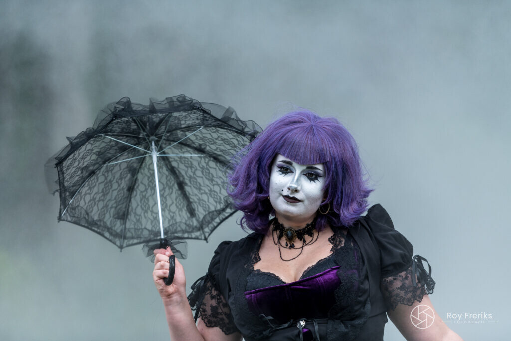 Vrouw met paars haar en witte schmink met een kanten parasol